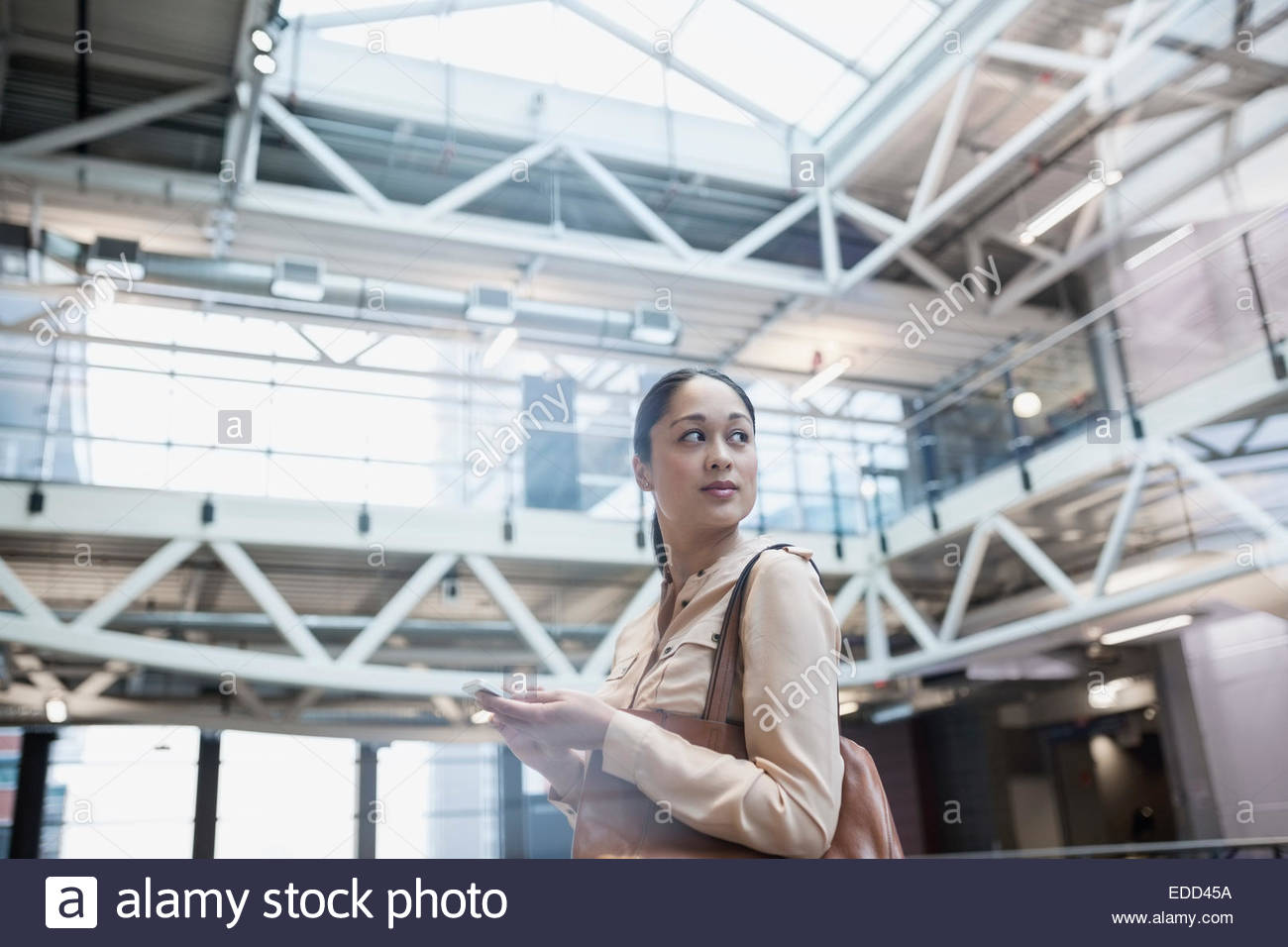 Businesswoman texting with cell phone in atrium Stock Photo - Alamy
