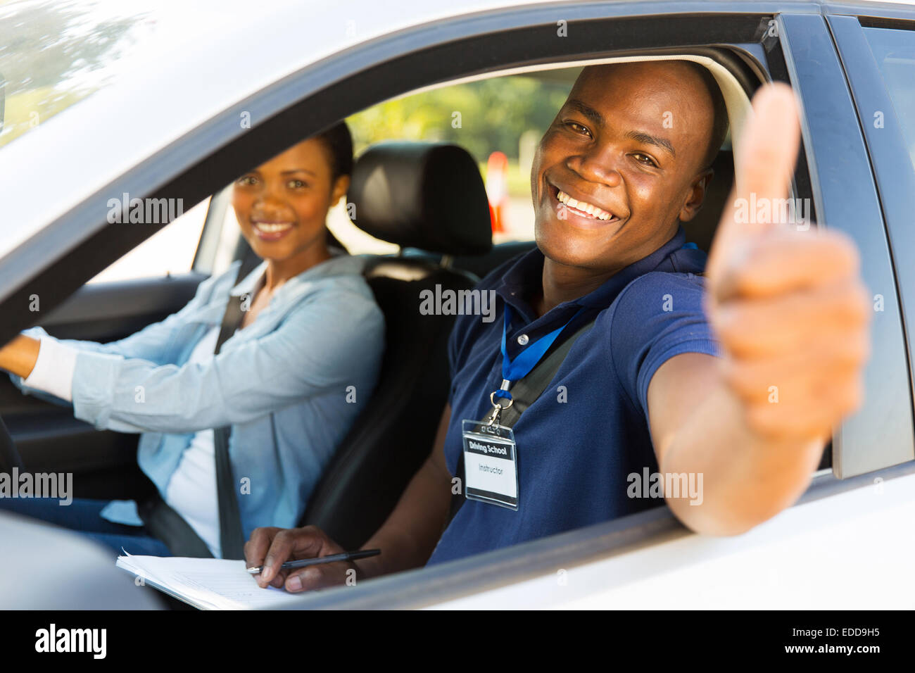happy male African driving instructor in a car with learner driver giving thumb up Stock Photo