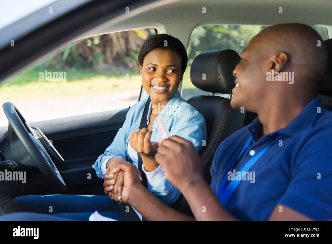cheerful woman being handed driver’s license by driving instructor in a car Stock Photo