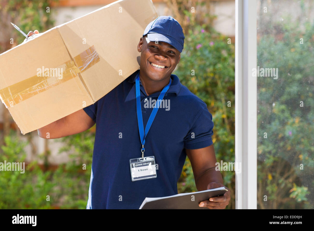 cheerful African courier standing with parcel at the door Stock Photo