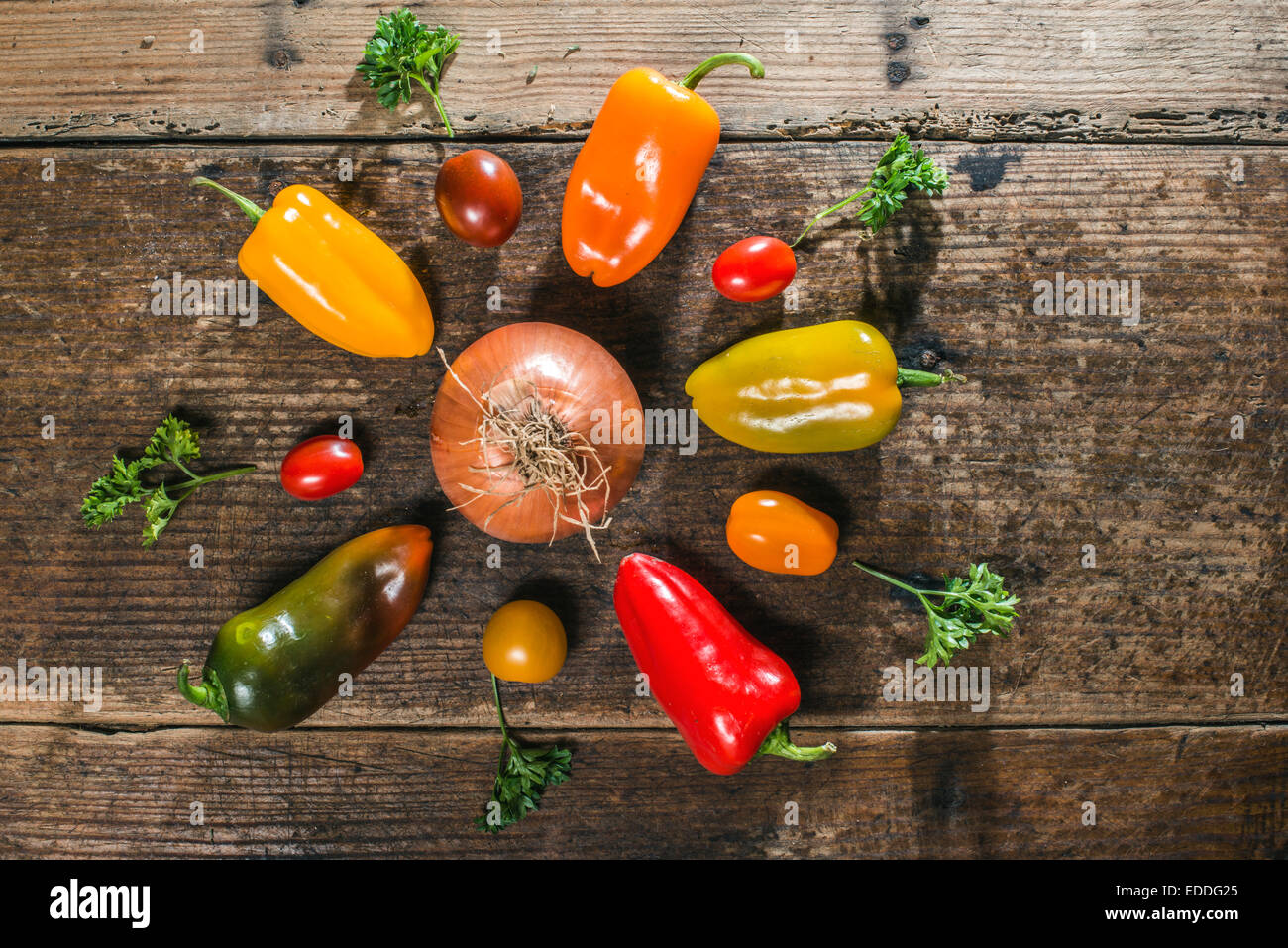 Multicolored peppers, cherry tomatoes, onion and parsley on wood Stock Photo