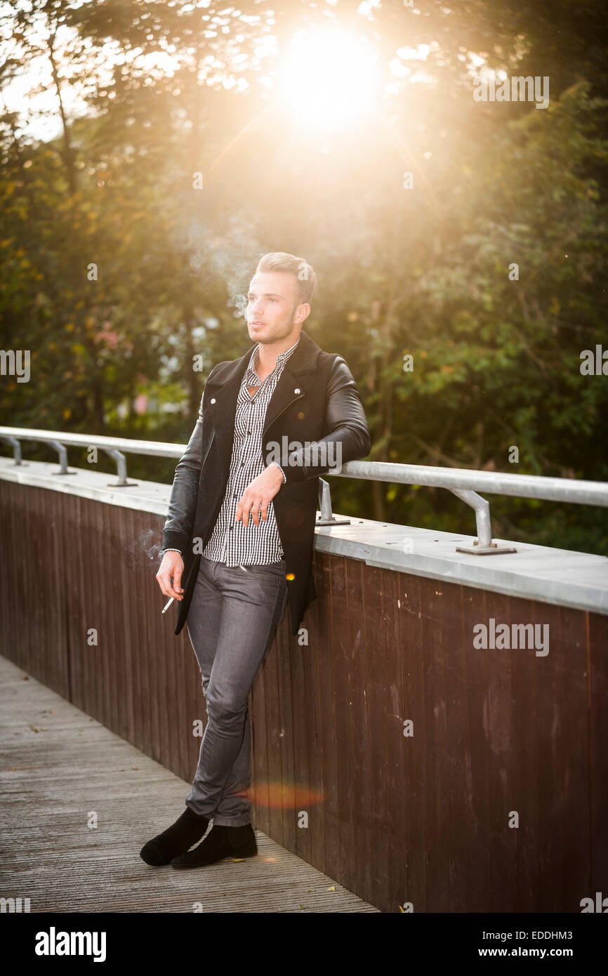 Young man smoking a cigarette on a footbridge at backlight Stock Photo