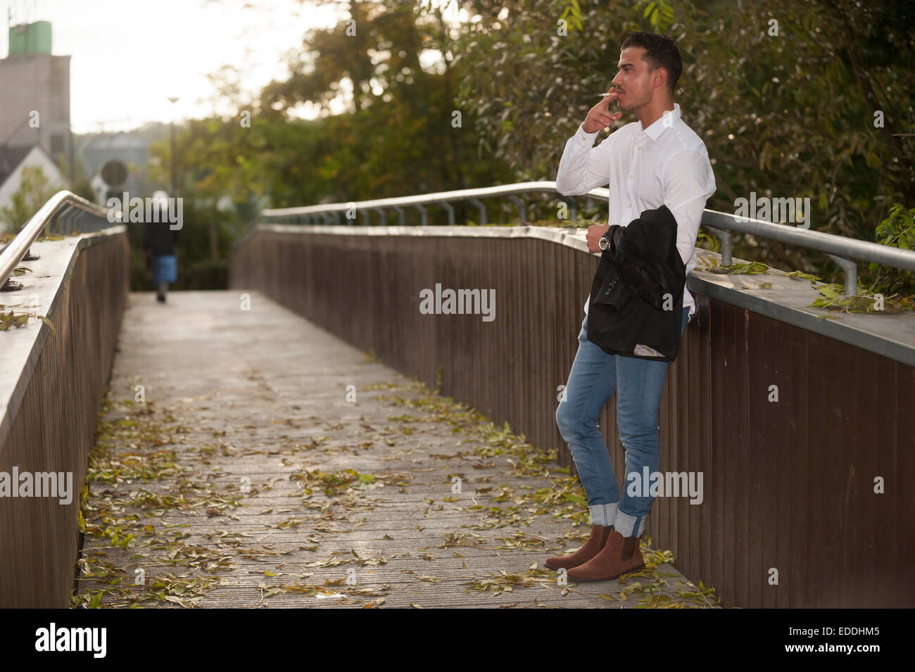 Stylish young man smoking a cigarette on a footbridge Stock Photo