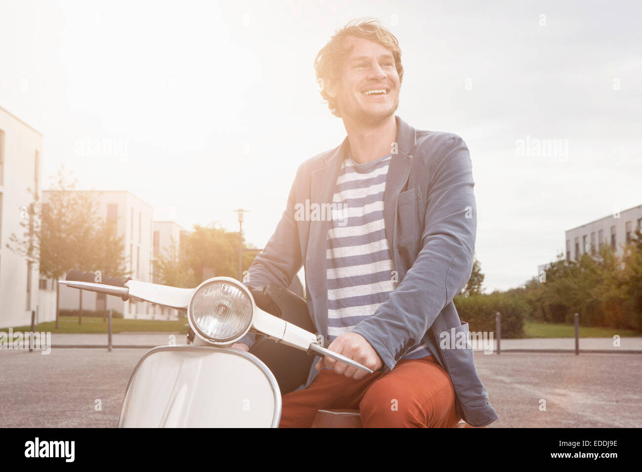 Smiling man sitting on his motor scooter at backlight Stock Photo