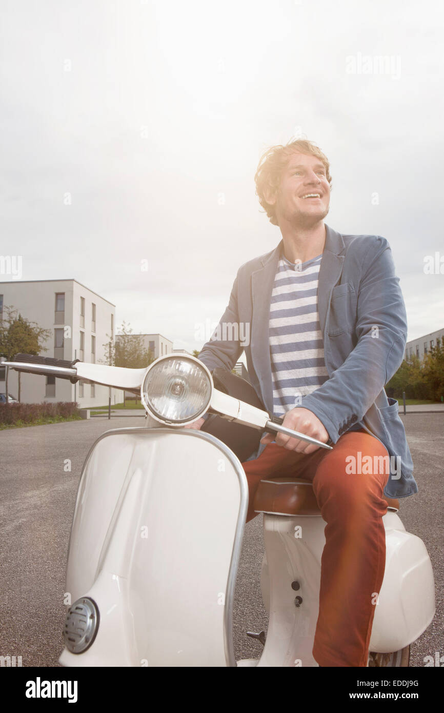 Smiling man sitting on his motor scooter at backlight Stock Photo