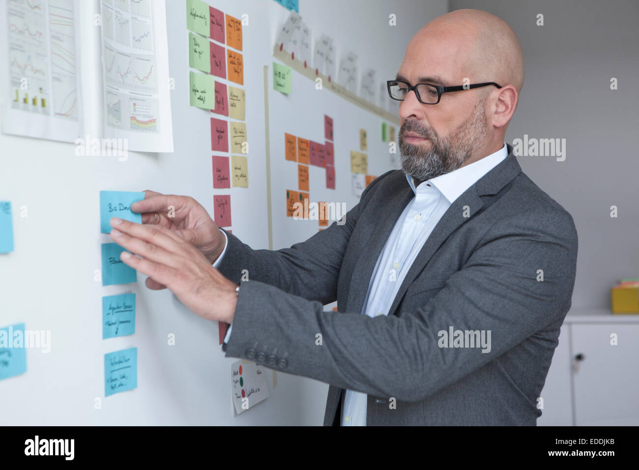 Businessman in office at wall with adhesive notes Stock Photo