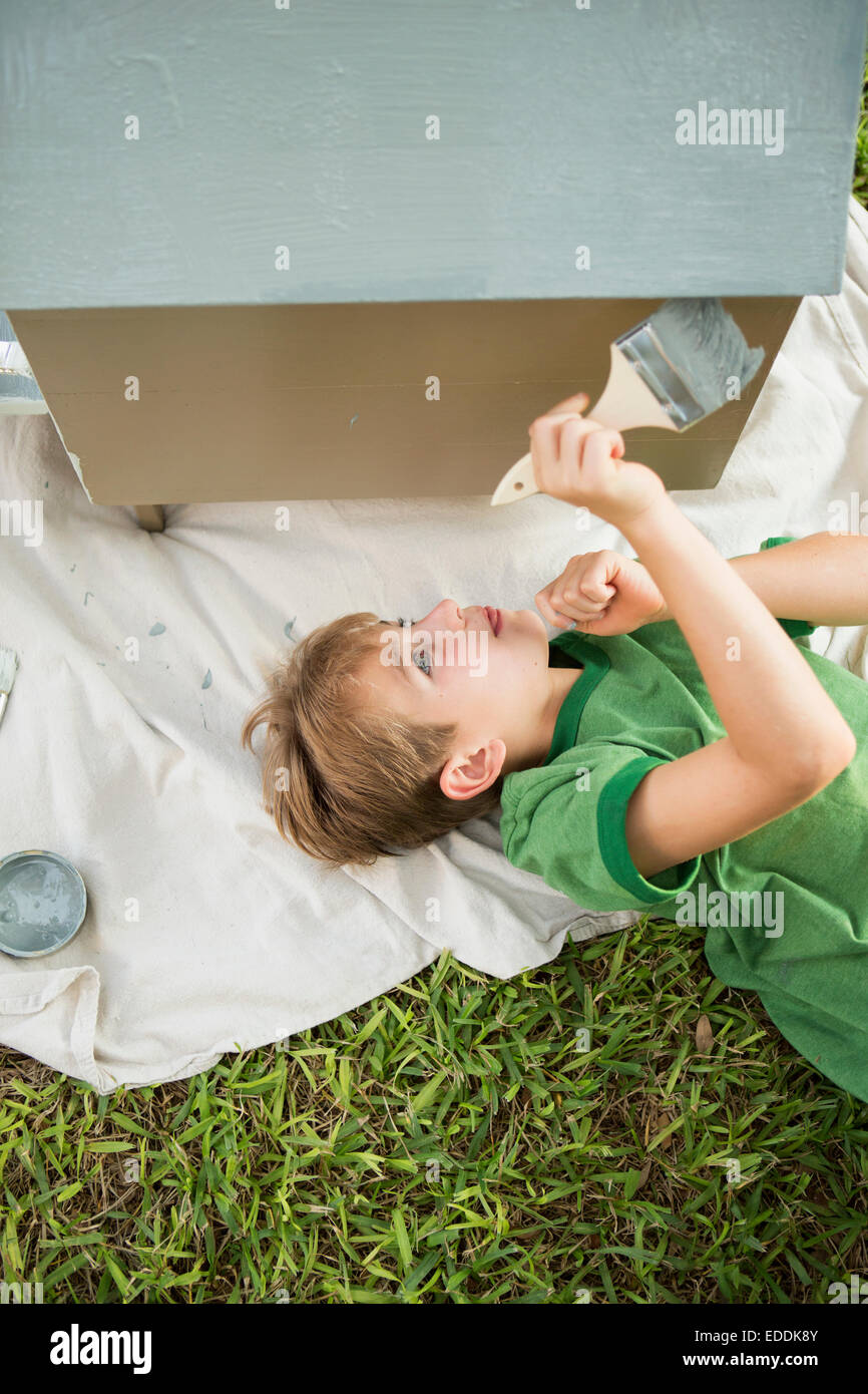 A boy in a garden, painting a dog house. Stock Photo
