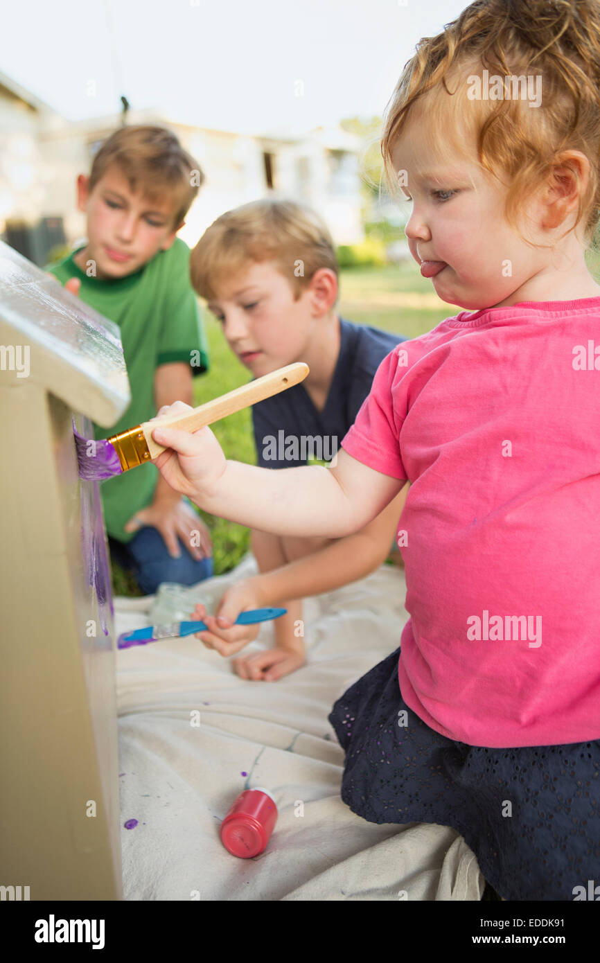 Three children in a garden, painting a dog house Stock Photo Alamy