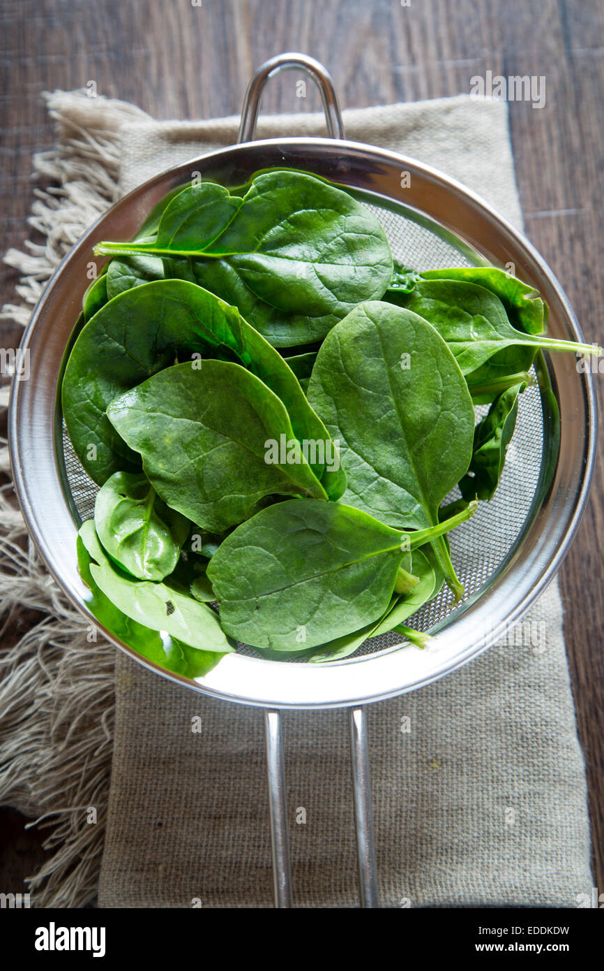 Strainer of fresh baby leaf spinach on cloth and wood Stock Photo
