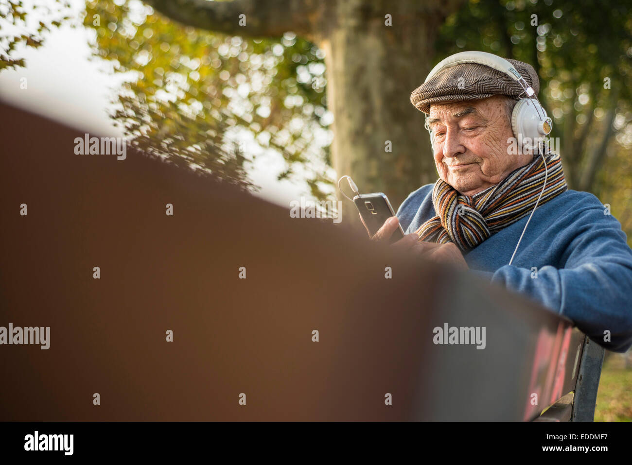 Senior man on park bench with cell phone and headphones Stock Photo