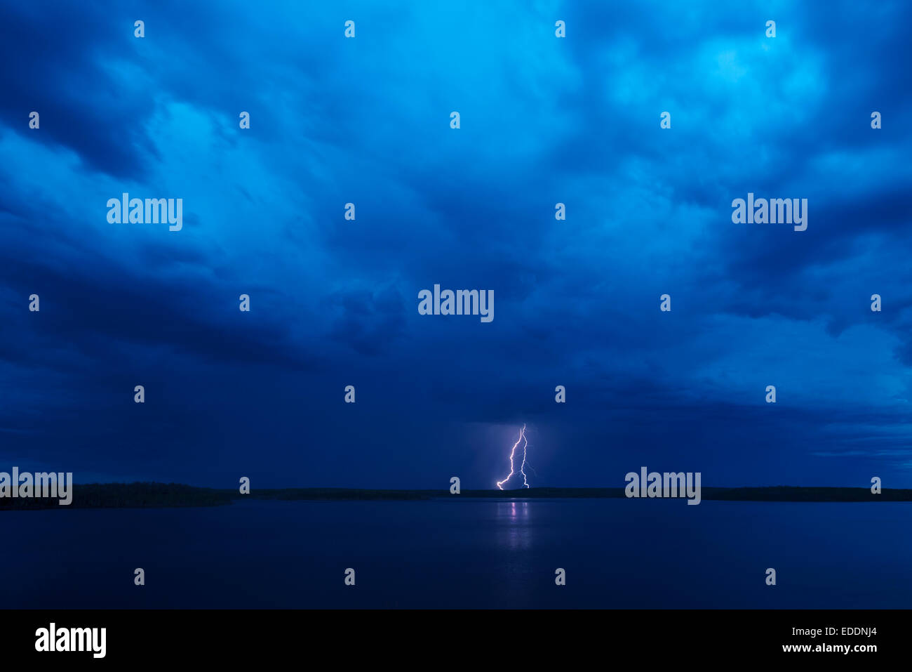 A lightning strike reflected in the water of a lake. Dark stormy ...