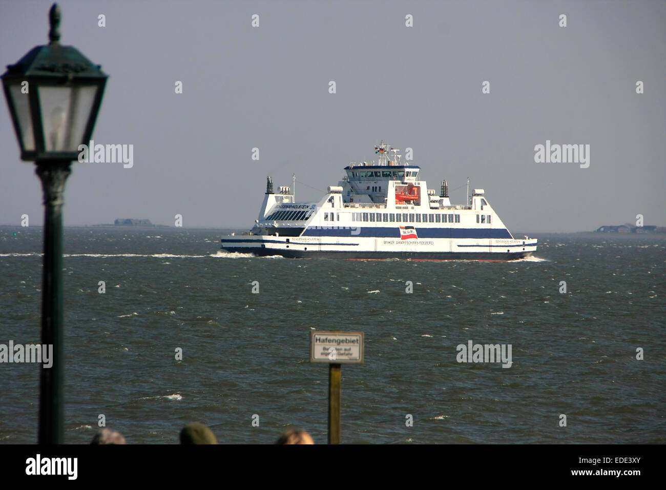 A ferry goes to the islets in the North sea in front Wyk. The promenade of Wyk runs parallel along the beach. Photo: Klaus Nowottnick Date: April 20, 2014 Stock Photo