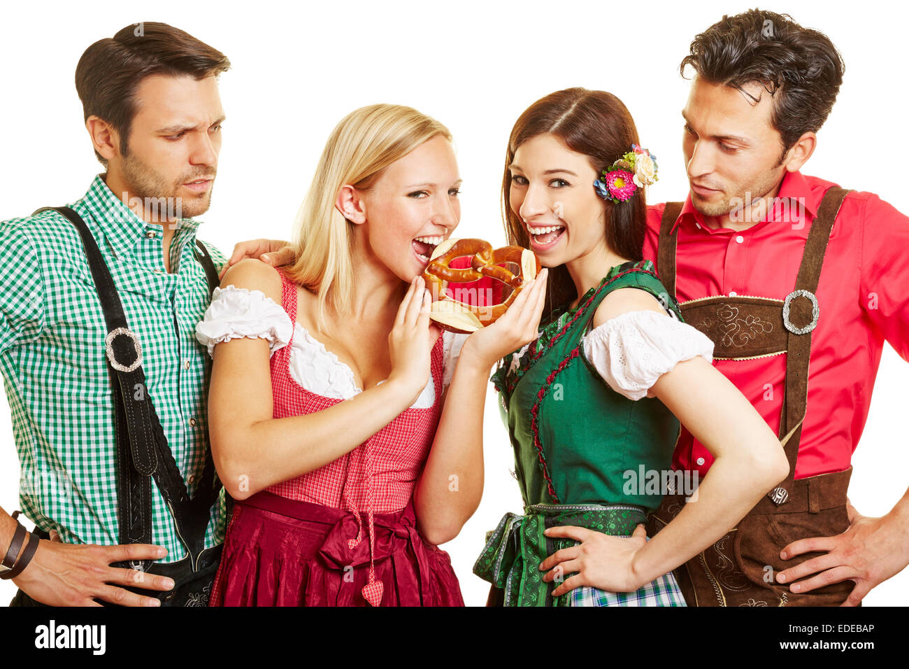 Two women in Bavaria eating a pretzel in front of their jealous men Stock Photo