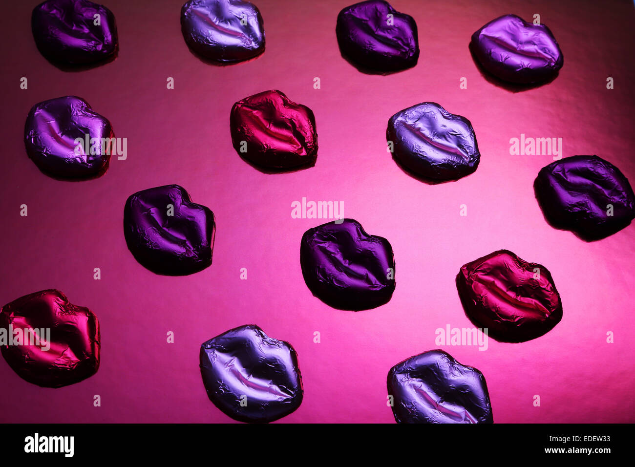 lip shaped metallic wrapper chocolates on pink metallic surface Stock