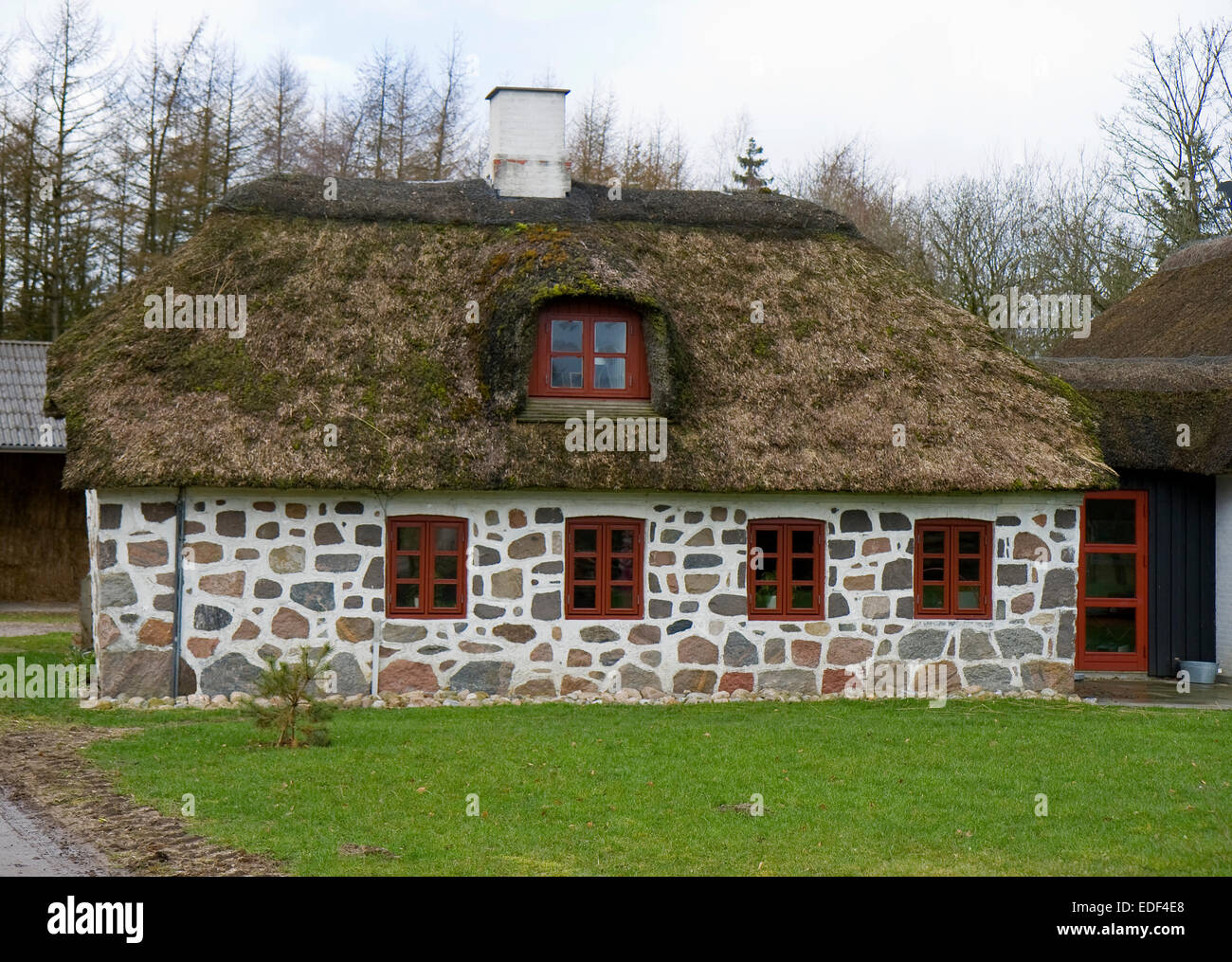 Small stone house with thatched roof and red windows Stock Photo