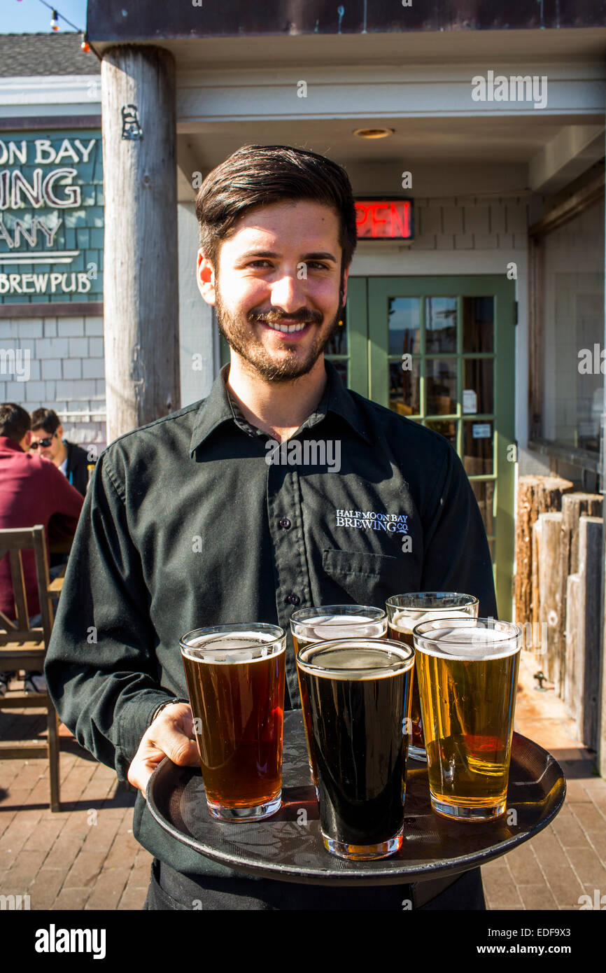 A server holds a variety of beers at Half Moon Bay Brewing Company in Half Moon Bay, California on a sunny day. Stock Photo