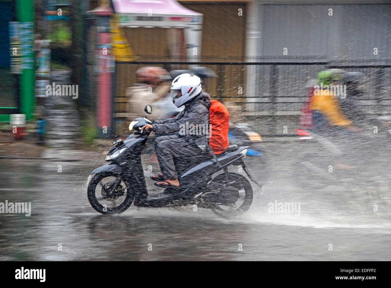 Soaked Indonesian biker riding on scooter during downpour in the rainy season in Kota Bandung, West Java, Indonesia Stock Photo