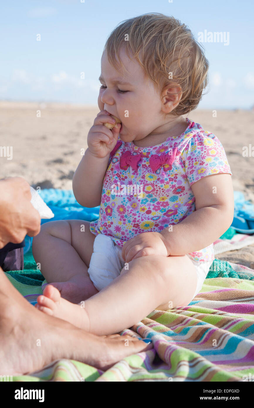 portrait of one year baby eating banana on towel next to mom at beach