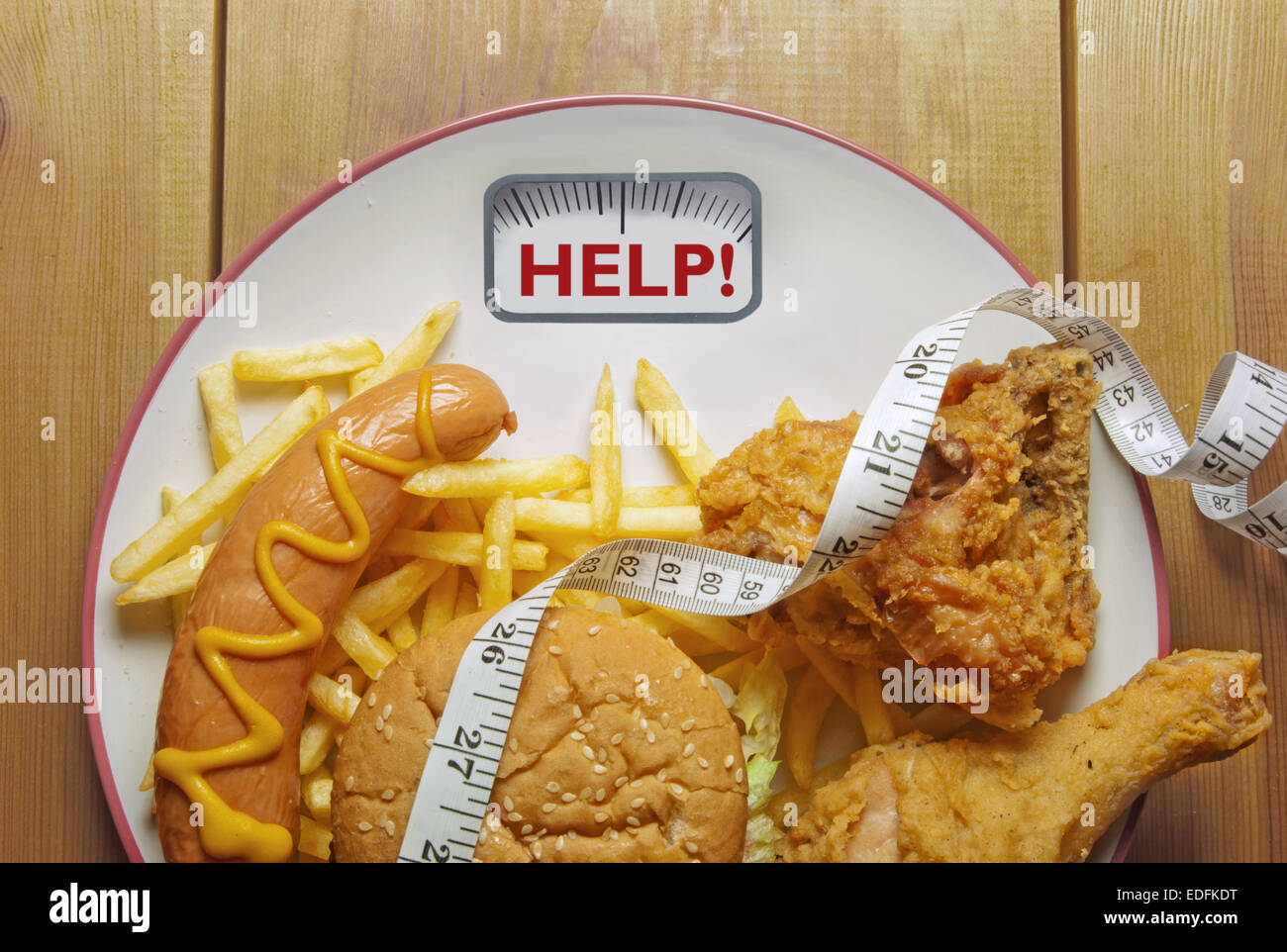 Plate with bathroom scales displaying the word help packed with junk food Stock Photo