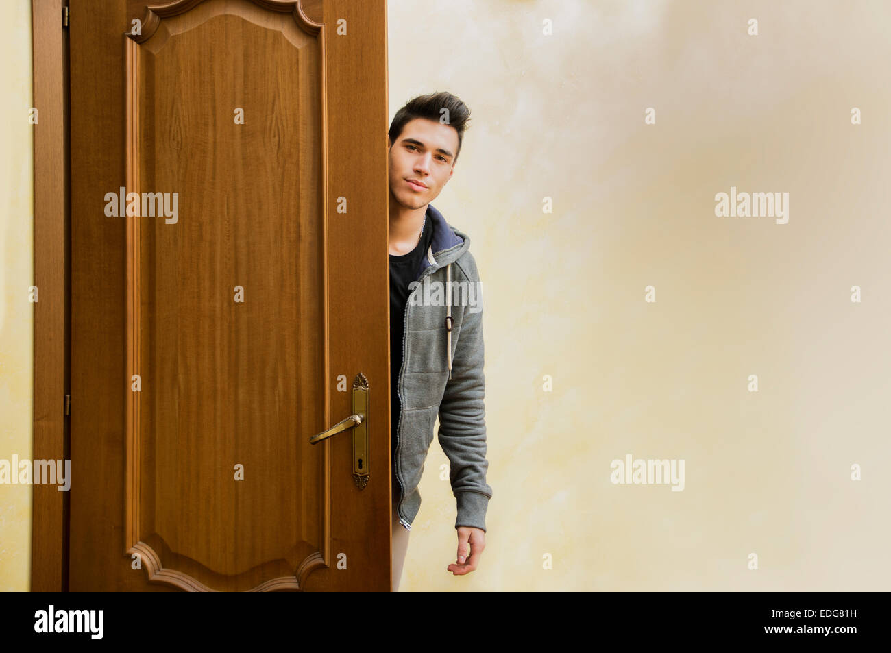 Handsome young man behind open door, getting out, looking at camera with friendly expression Stock Photo