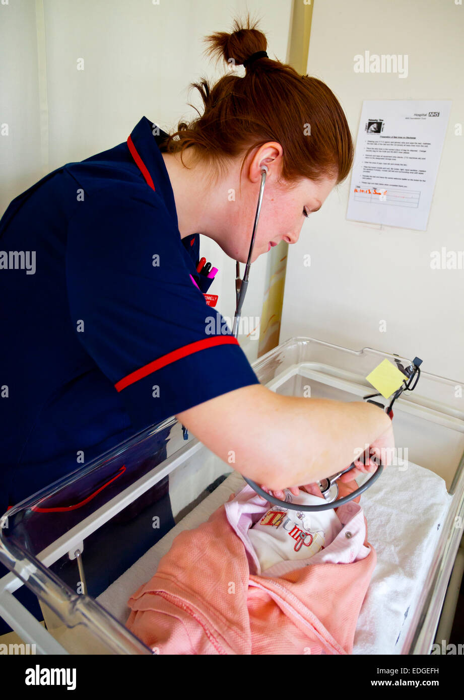 NHS Midwife in a British hospital examining a new born baby in a cot