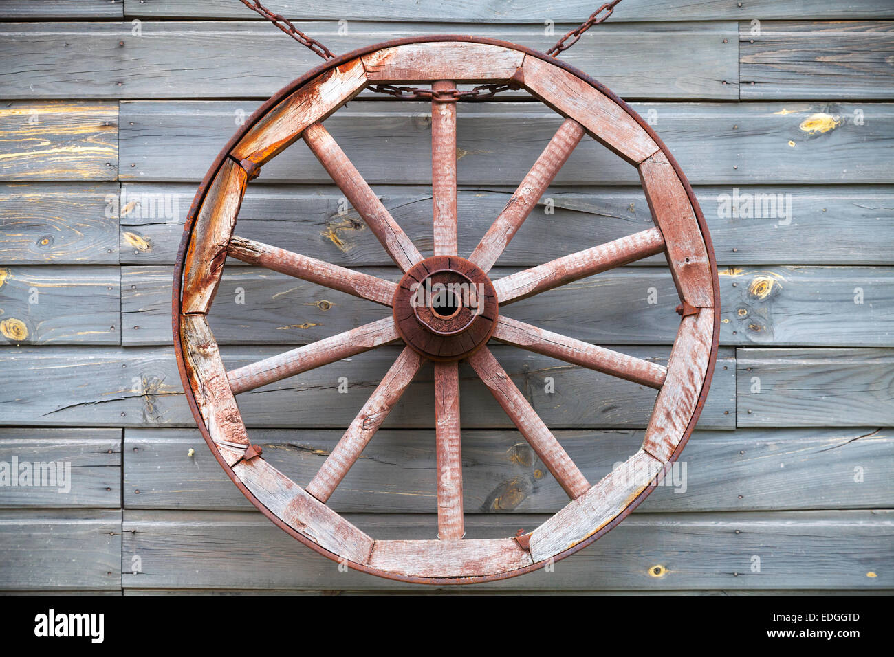 Old used wooden wheel hanging on rural wall background Stock Photo