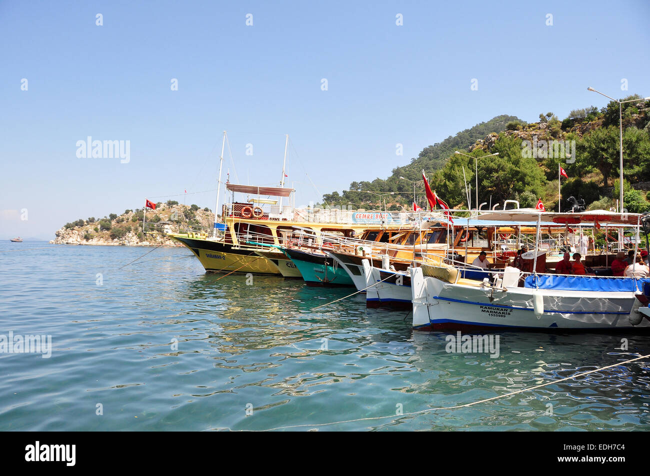 Wooden tourist boats from Marmaris  line up in the harbour at Turunc whilst tourists visit the local market. Stock Photo