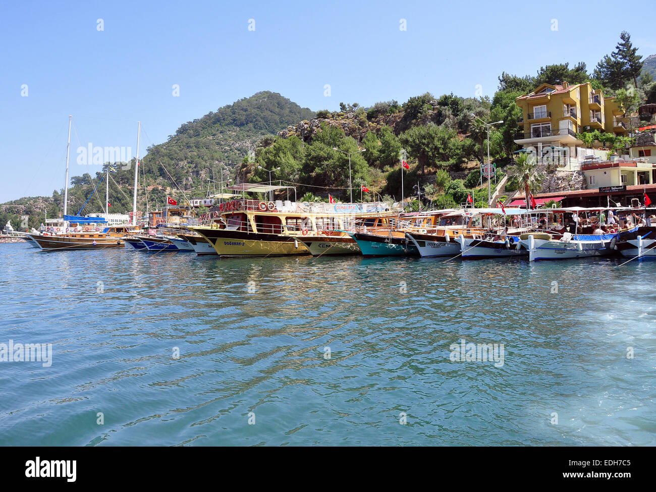 Wooden tourist boats from Marmaris  line up in the harbour at Turunc whilst tourists visit the local market. Stock Photo