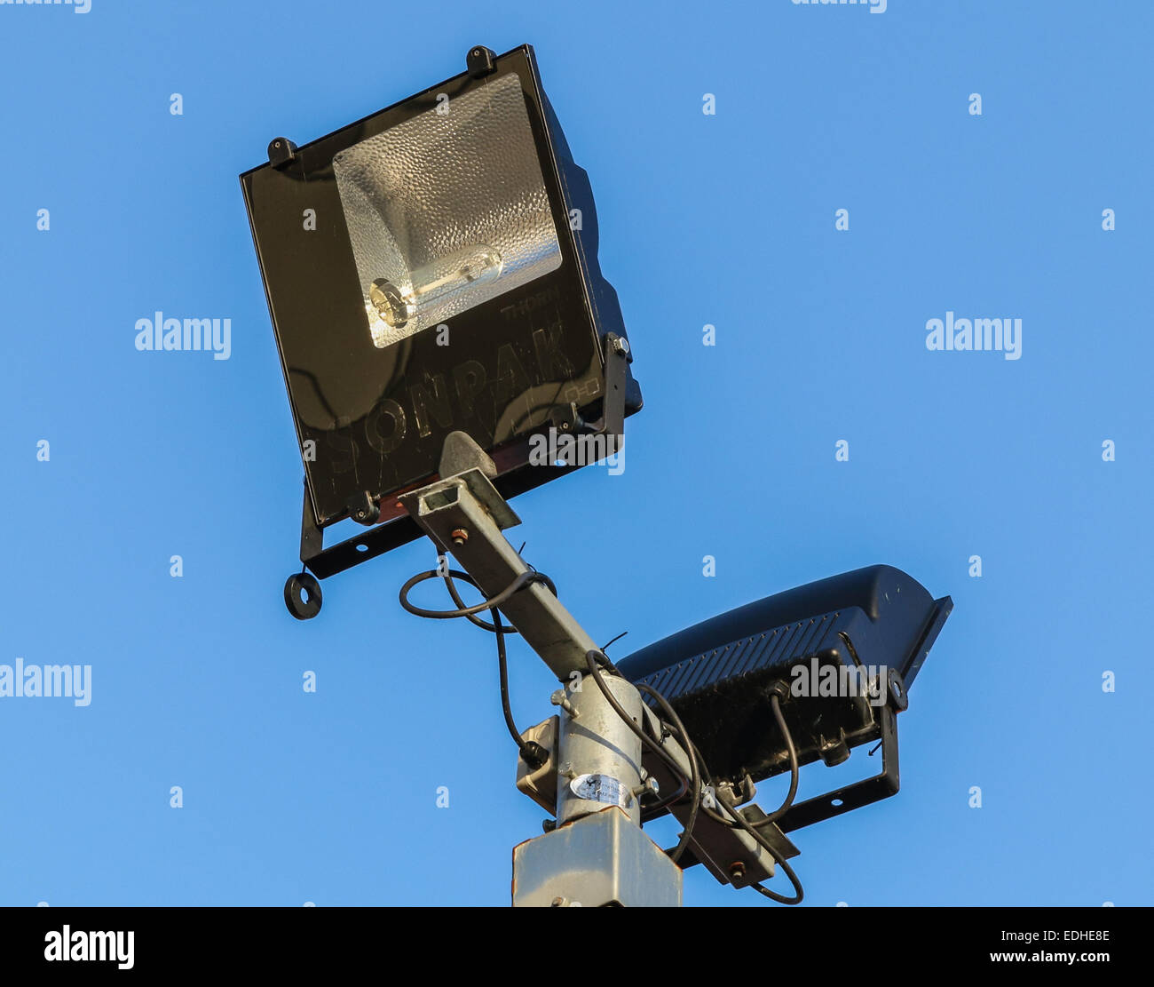 Security floodlights on a tall post against a winter blue sky at a UK shopping centre or shopping mall. Stock Photo