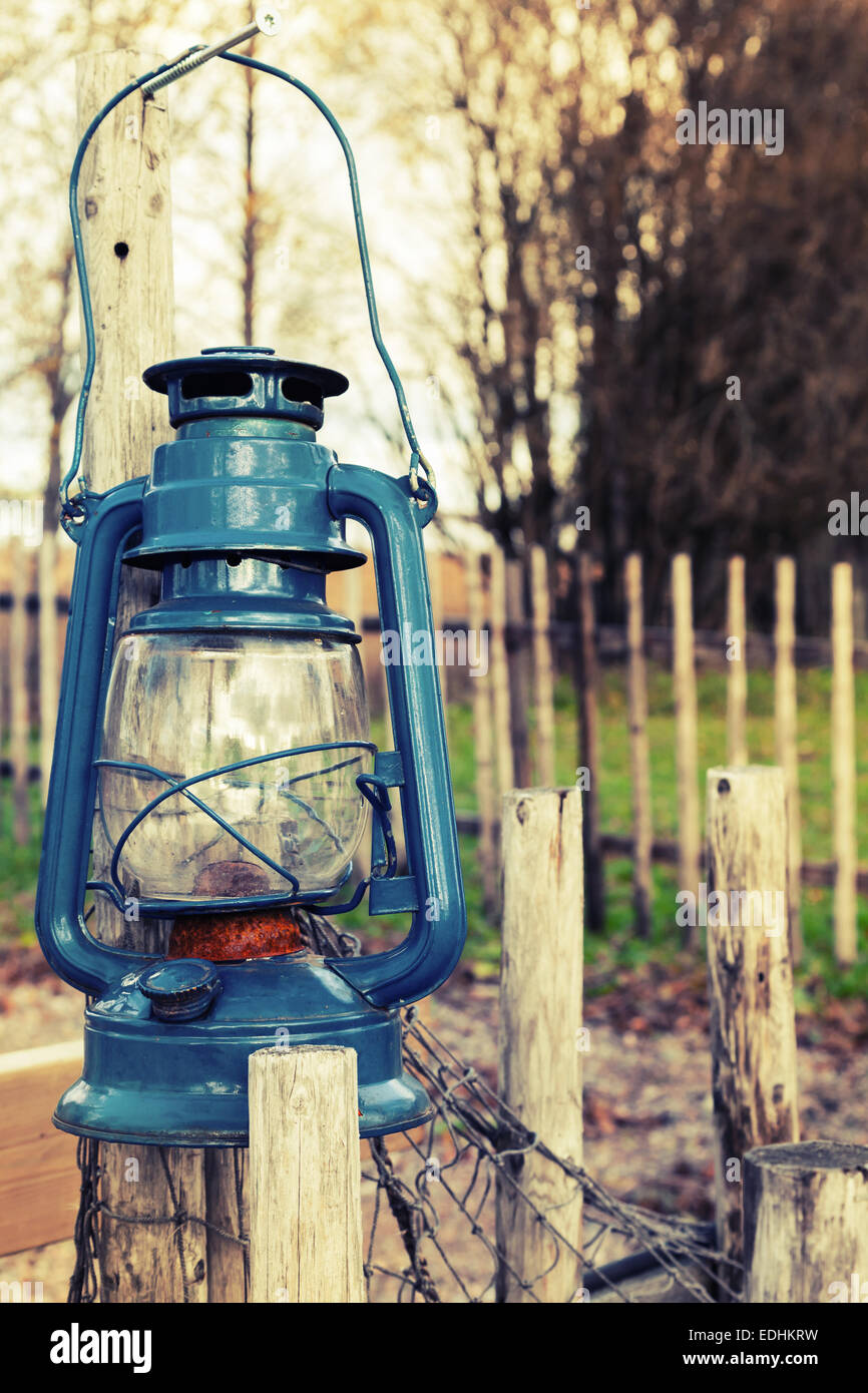 Old blue kerosene lamp hangs on wooden outdoor fence, vintage toned photo with filter effect Stock Photo