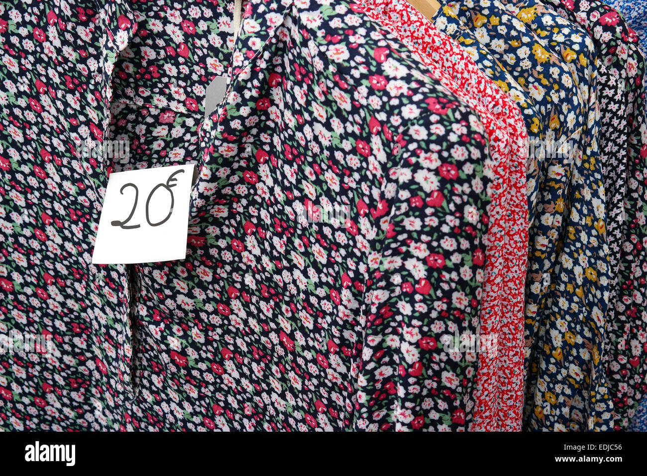Hand writted price tag on clothes rack with floral dresses at a market stall Stock Photo