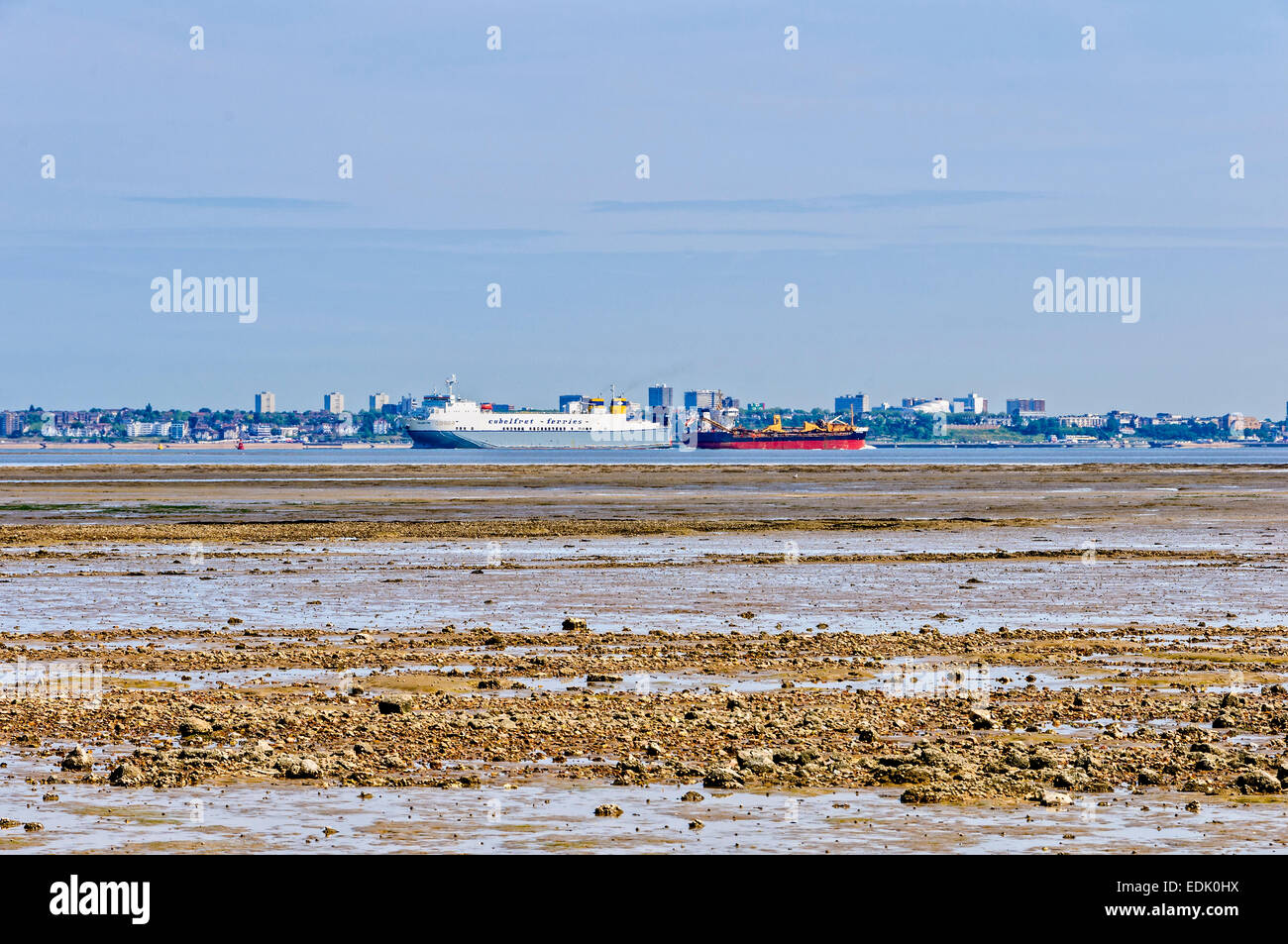 Two ships sail in opposite directions on a tranquil River Thames bordered by a shingle muddy beach and a green urban landscape Stock Photo