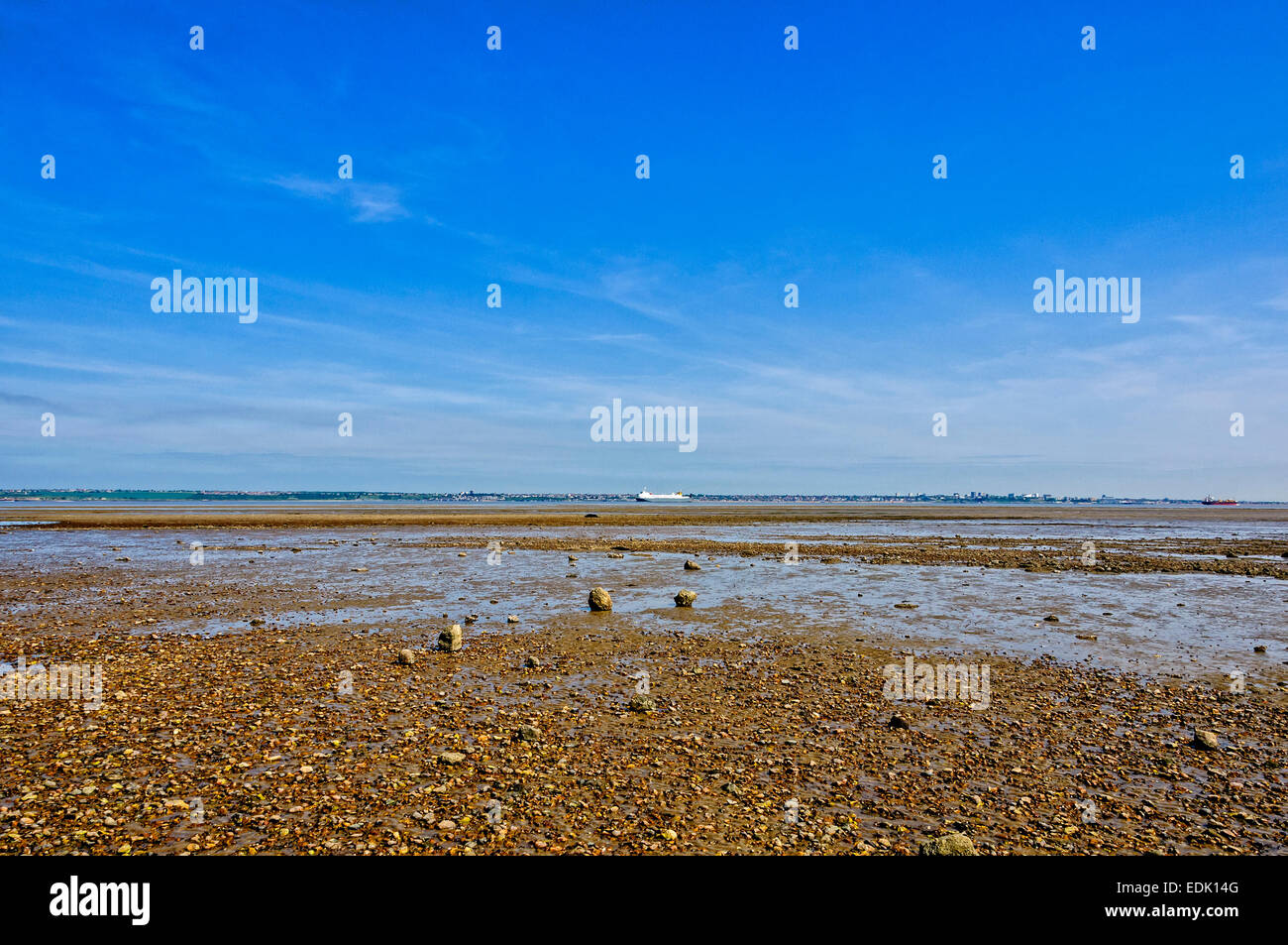 Two ships sail in opposite directions on a tranquil River Thames past a shingle muddy beach under an intense blue sky Stock Photo
