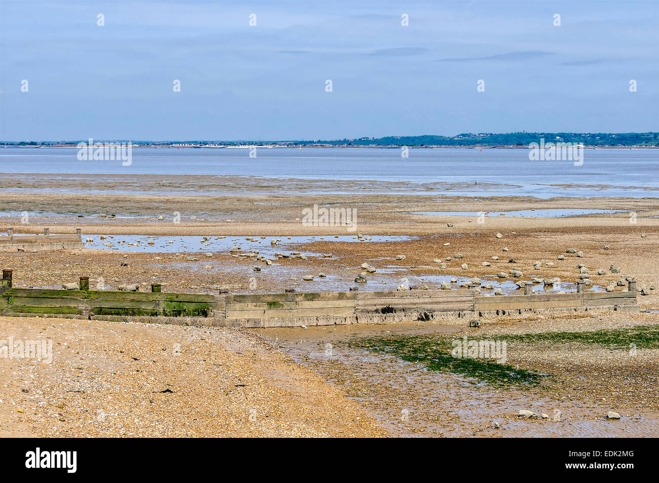 A tranquil River Thames flows past a muddy shingle beach on one bank and industrial and domestic buildings on the other shore Stock Photo