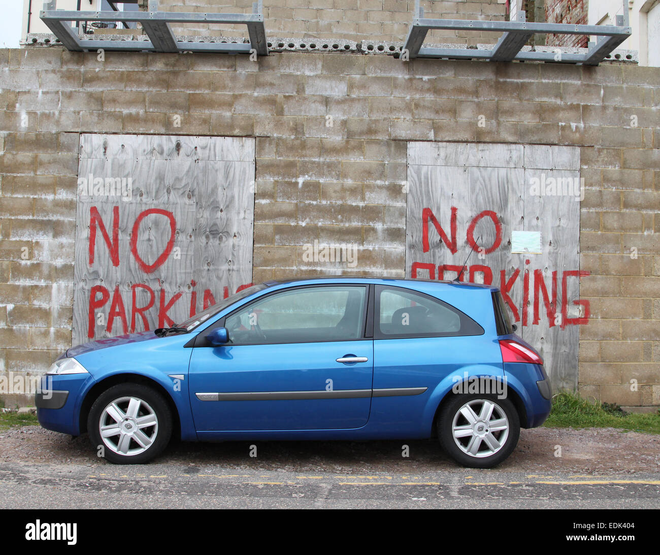 Car parked in front of 'no parking' painted sign on brick wall and boards Stock Photo