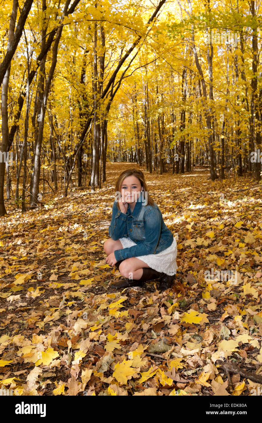 full length portrait of young female teen kneeling on forest trail in autumn Stock Photo
