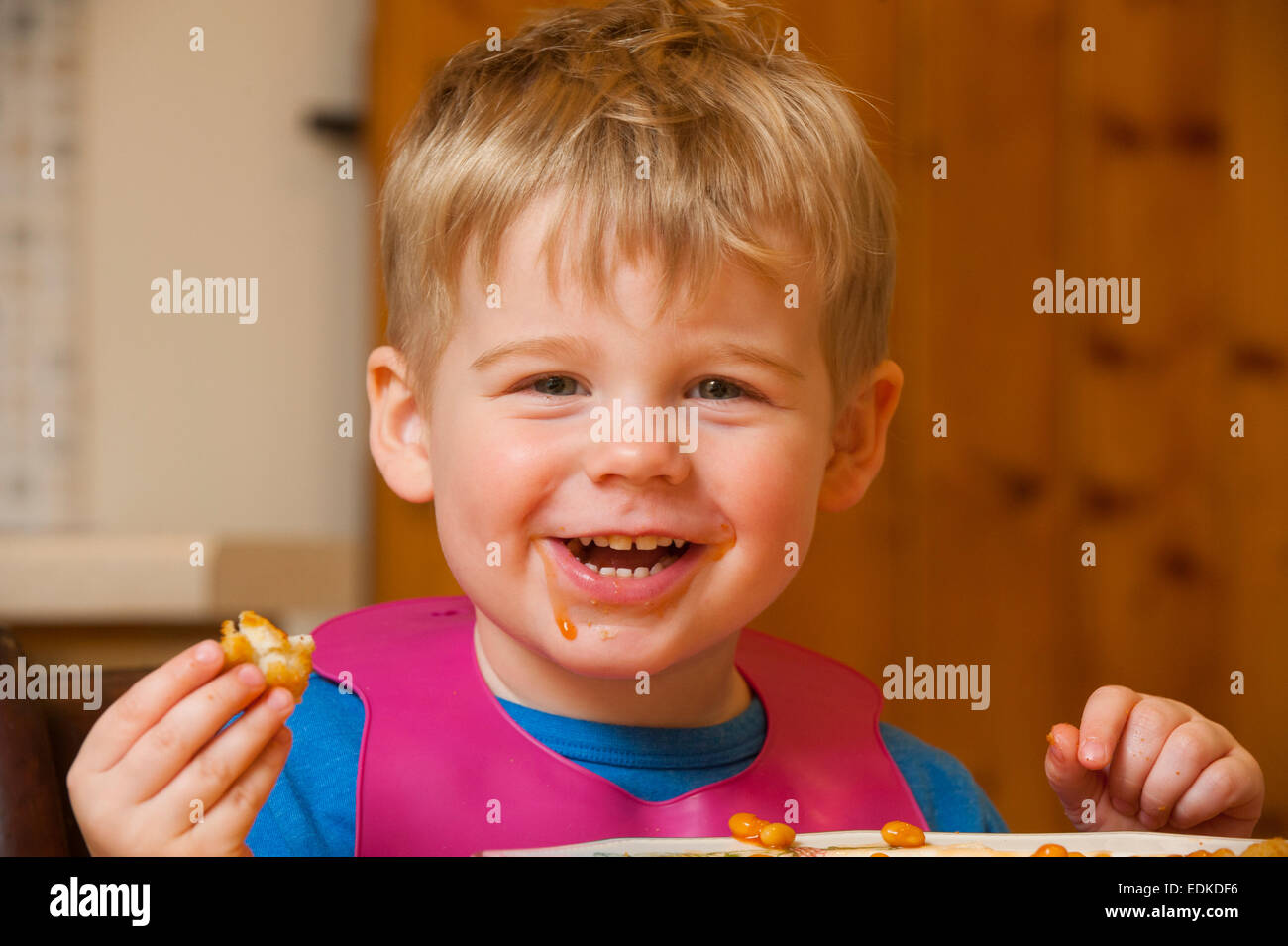 A happy two year old child eating chicken nuggets and baked beans. Stock Photo