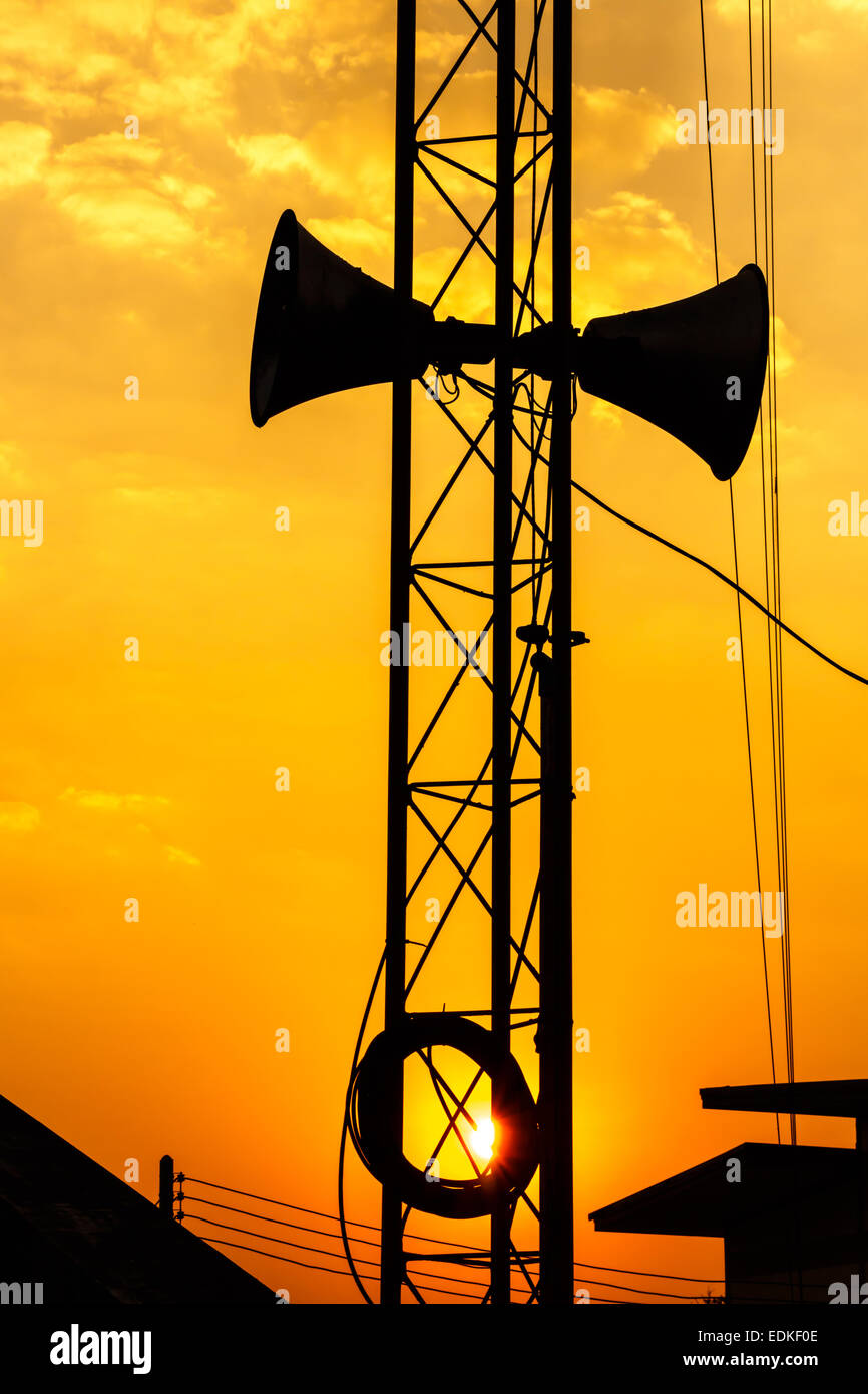 loudspeaker on metal pillar above roof of house in twilight time at Thailand (silhouette style) Stock Photo