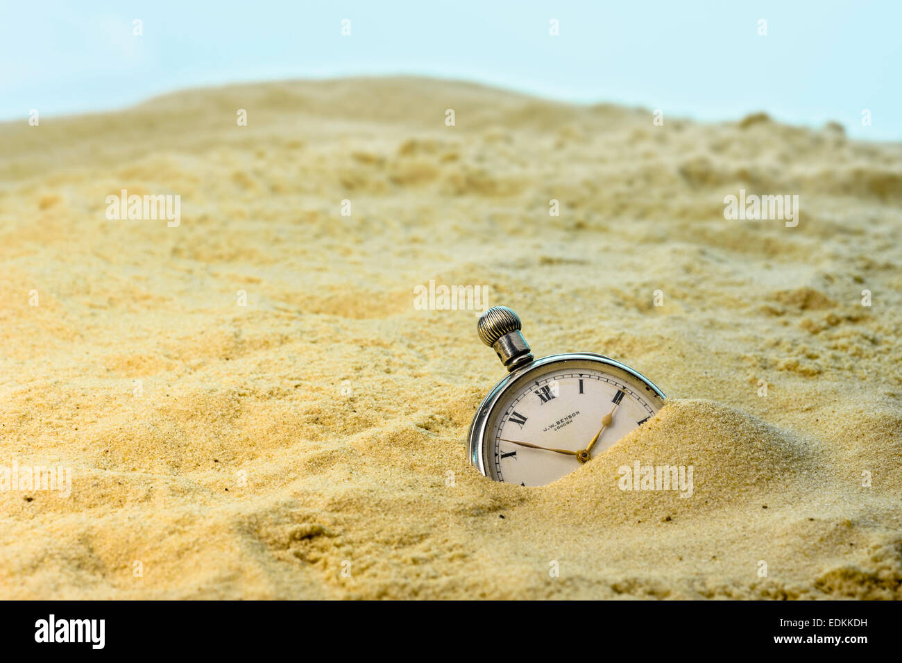 Pocket watch buried in a sandy beach. Stock Photo