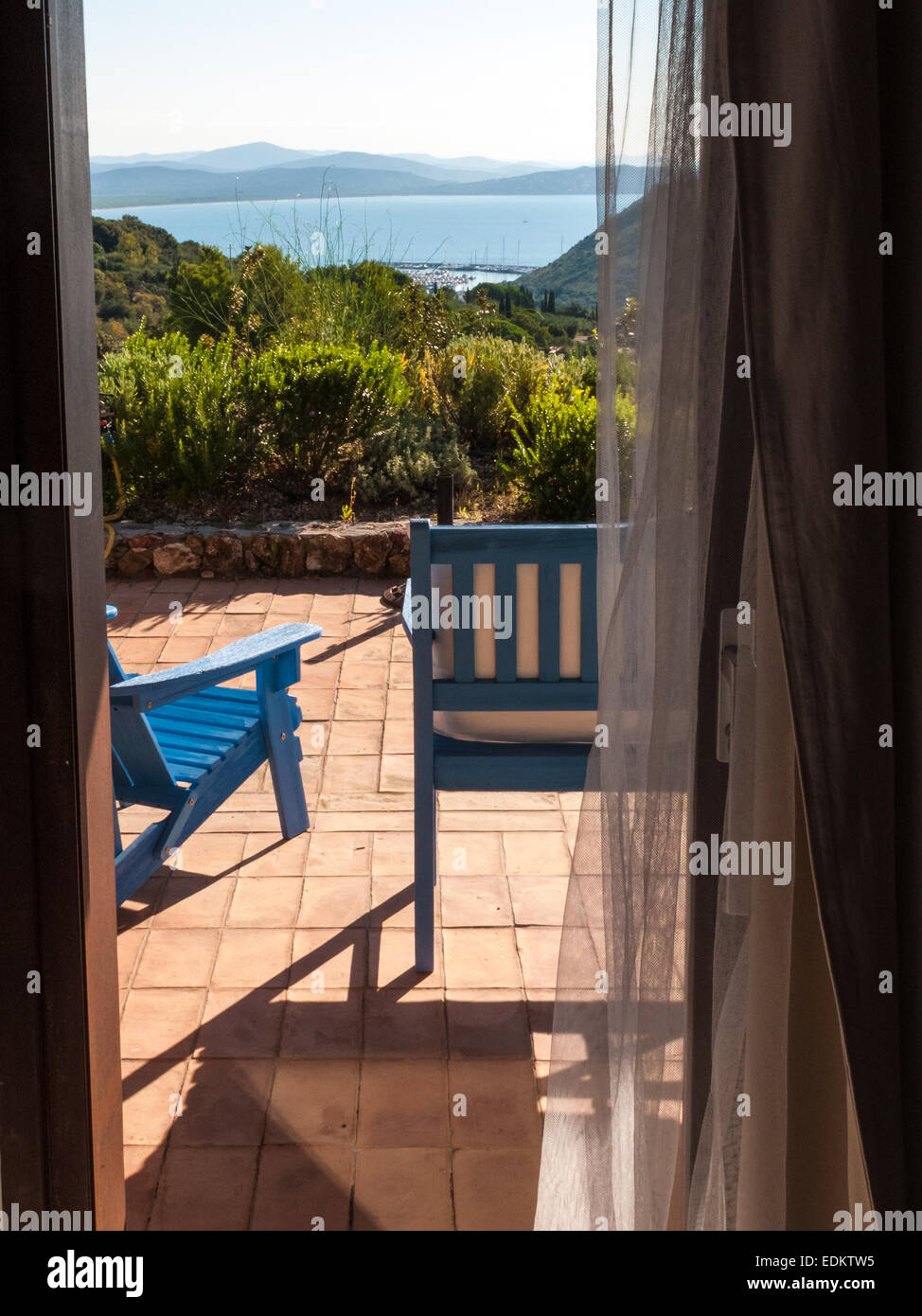 two blue wooden deckchairs on the patio of a villa on the sea views ...