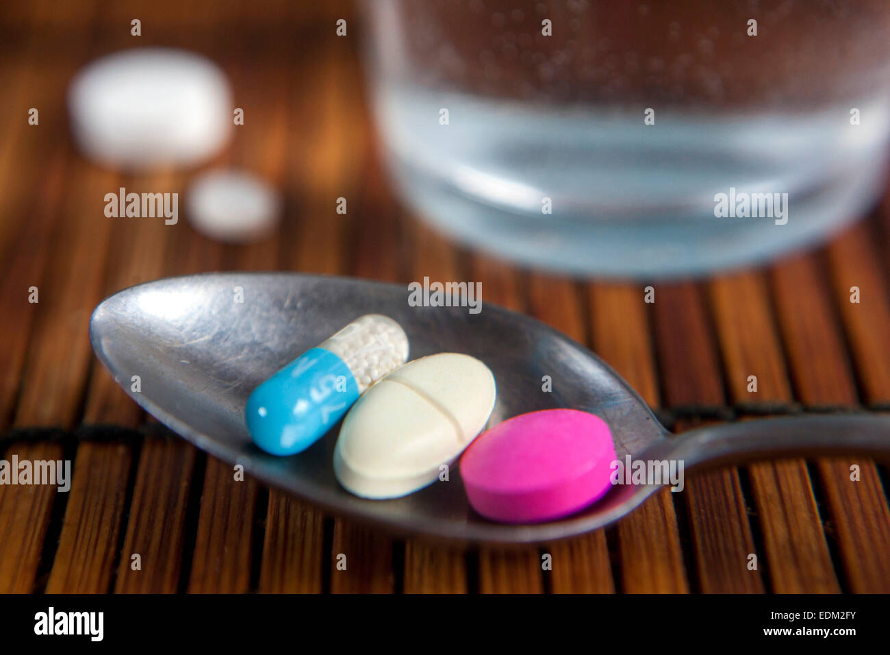 pills on a spoon and a glass of water Stock Photo