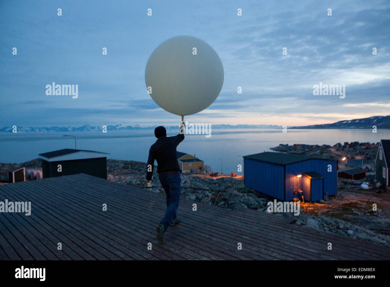 Man releasing a weather balloon over Ittoqqortoormiit, Scoresby Sund, East Greenland. Stock Photo