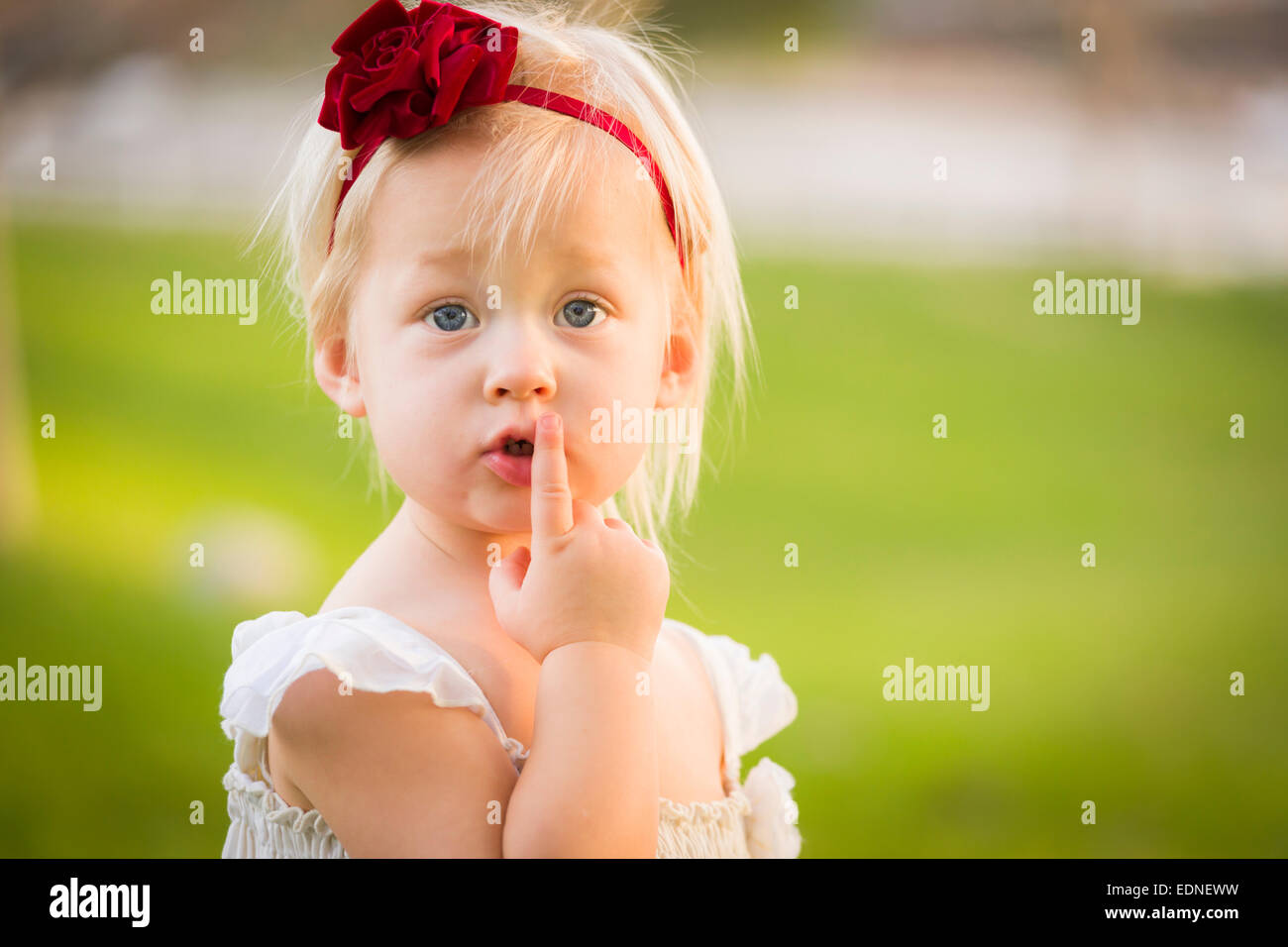Beautiful Adorable Little Girl With Her Finger on Her Mouth Wearing White Dress In A Grass Field. Stock Photo