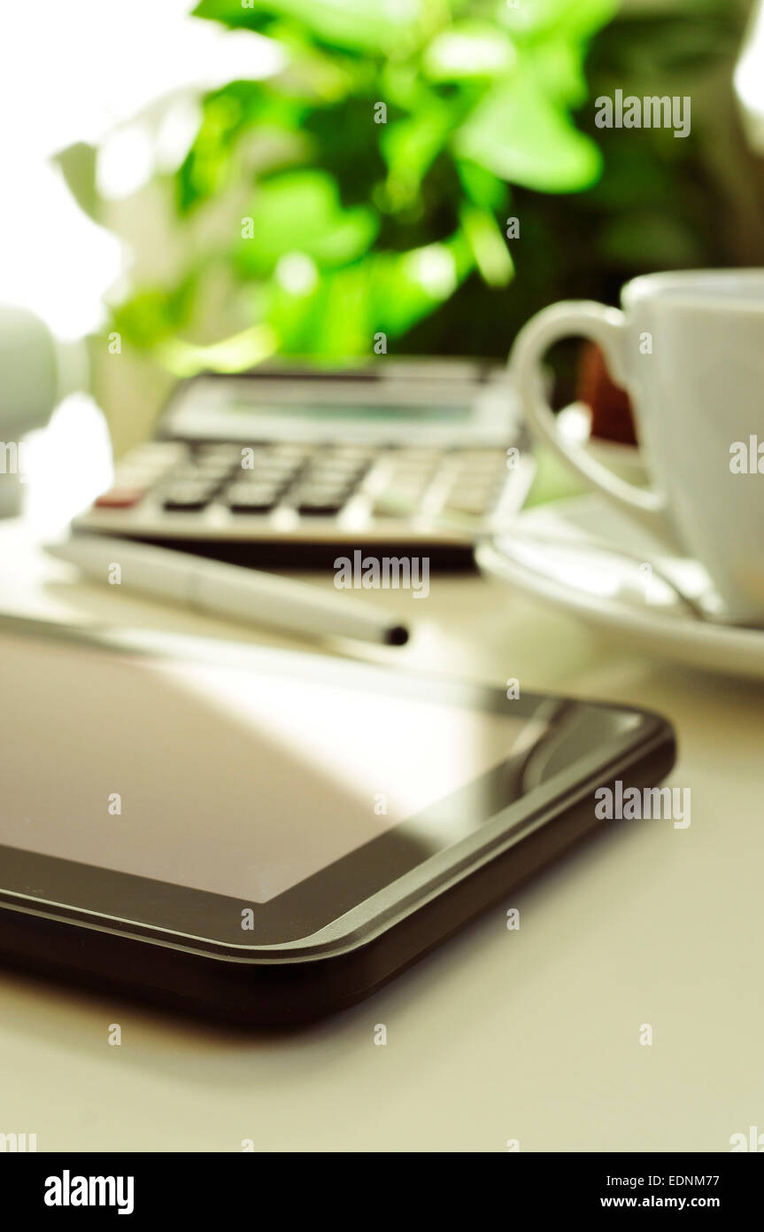 detail of a desk with a tablet, a calculator and a cup of coffee or tea in a home office Stock Photo