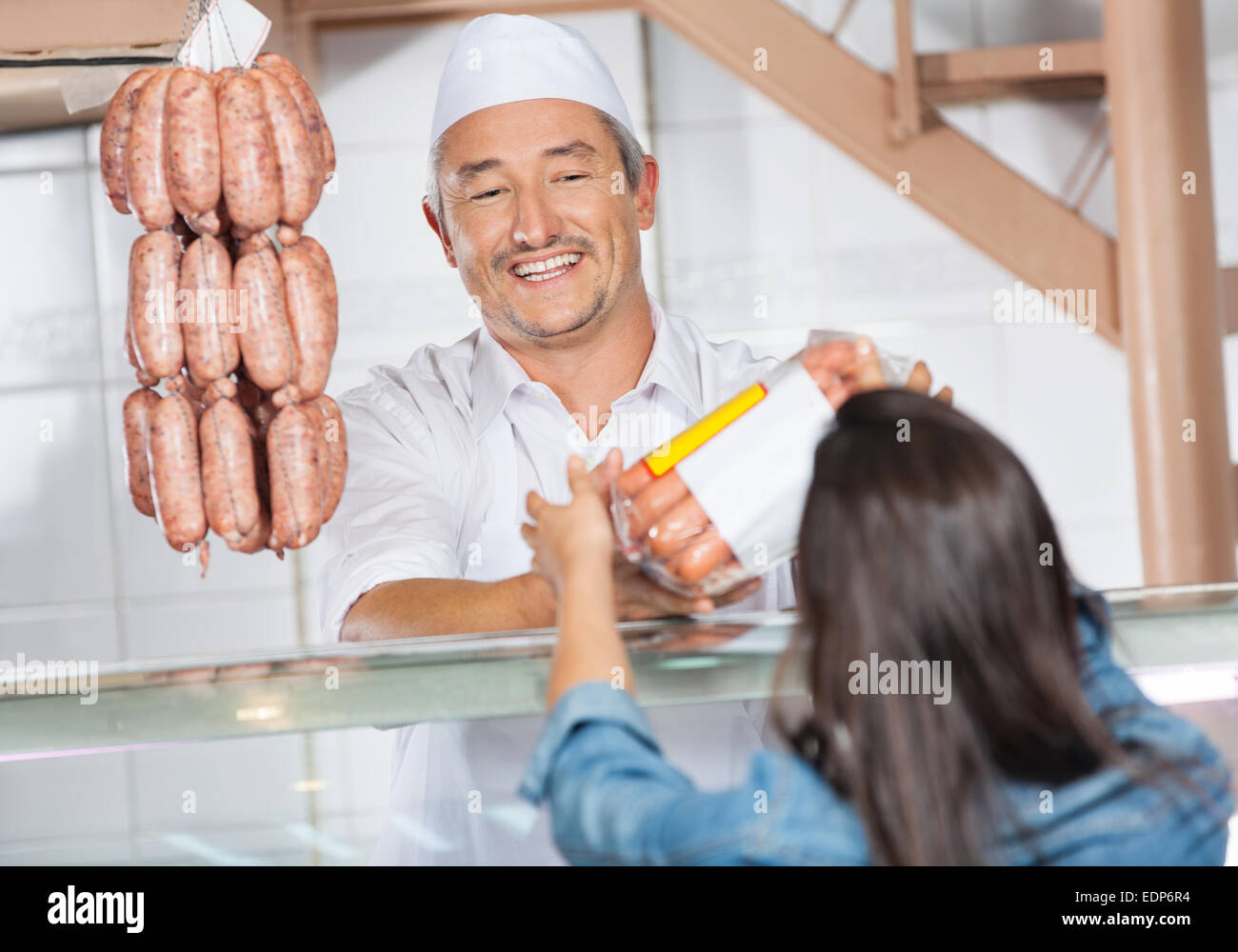 Butcher Giving Packed Sausages To Female Customer Stock Photo