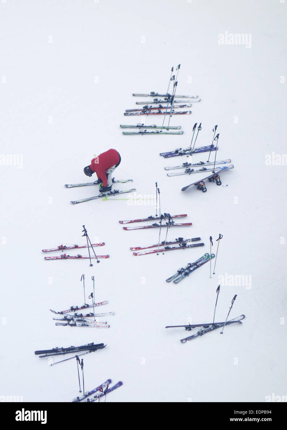 aerial view of man wearing red jacket surrounded by abandoned sets of skis and poles in the snow Stock Photo