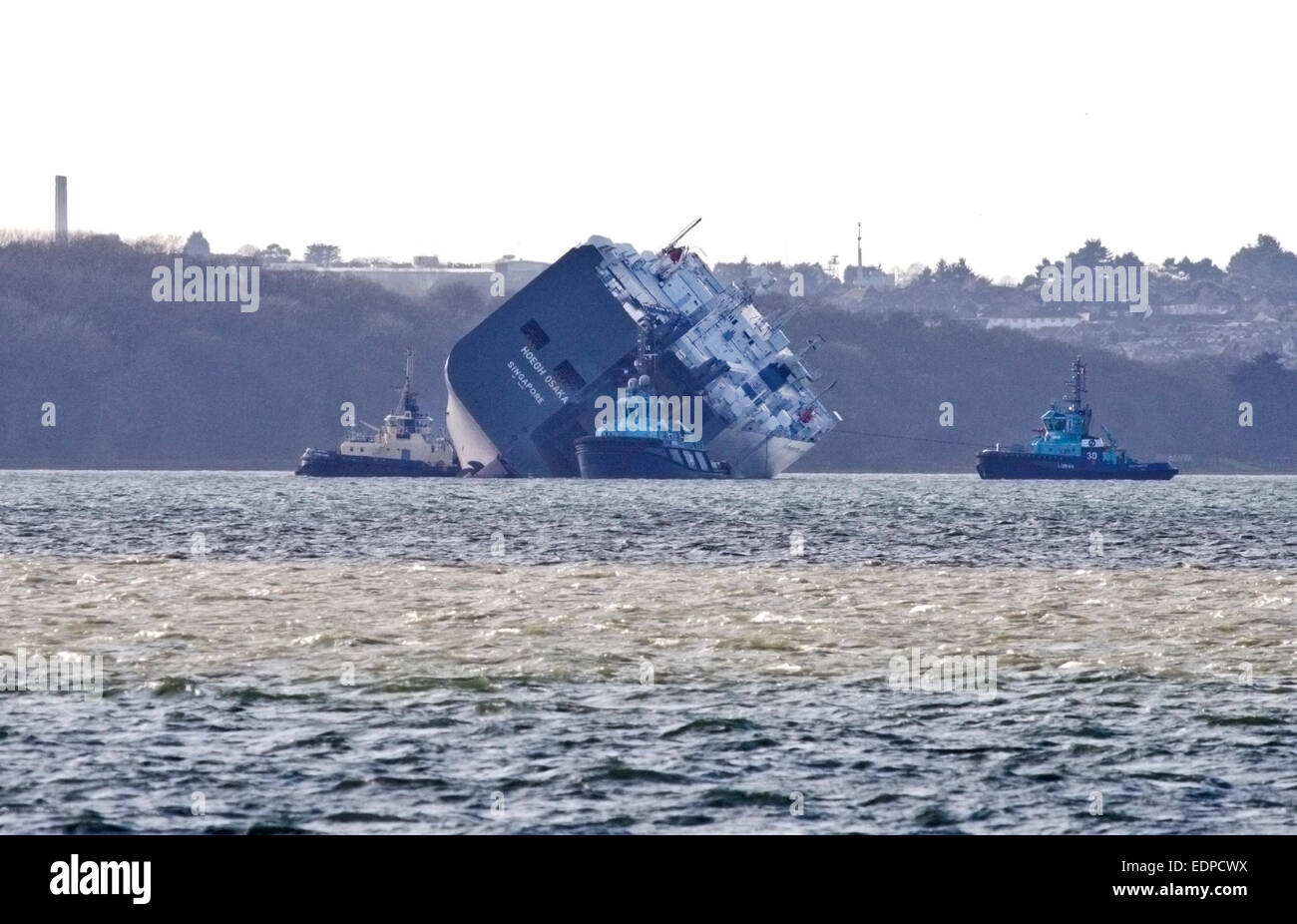 Solent, UK. 12:58pm on 8 January 2015 Hoegh Osaka Car Transporter off Cowes, having been towed 2 miles from Bramble Bank in the Solent where she ran aground on 3 January 2015, has now begun to be turned by tug boats to prevent disruption to the shipping lane.  The tug boat on the right is using a rope to turn the vessel while the other tugs appear to be nudging it. Credit:  Krys Bailey/Alamy Live News Stock Photo