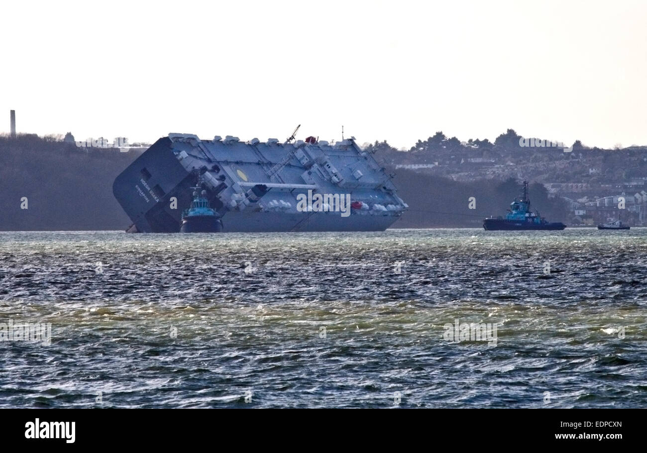 Solent, UK. 12:59pm on 8 January 2015 - Hoegh Osaka Car Transporter off Cowes, having been towed 2 miles from Bramble Bank in the Solent where she ran aground on 3 January 2015, has now begun to be turned by tug boats to prevent disruption to the shipping lane.  The tug boat on the right is using a rope to turn the vessel while the other tugs appear to be nudging it. Credit:  Krys Bailey/Alamy Live News Stock Photo