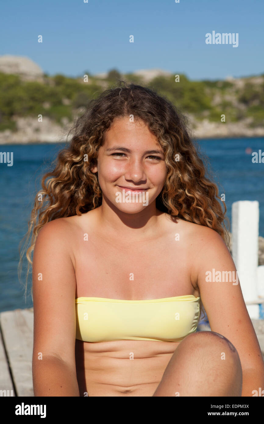 Happy tanned Caucasian teenager girl seated on a wooden dock in a Greek bay  Stock Photo - Alamy