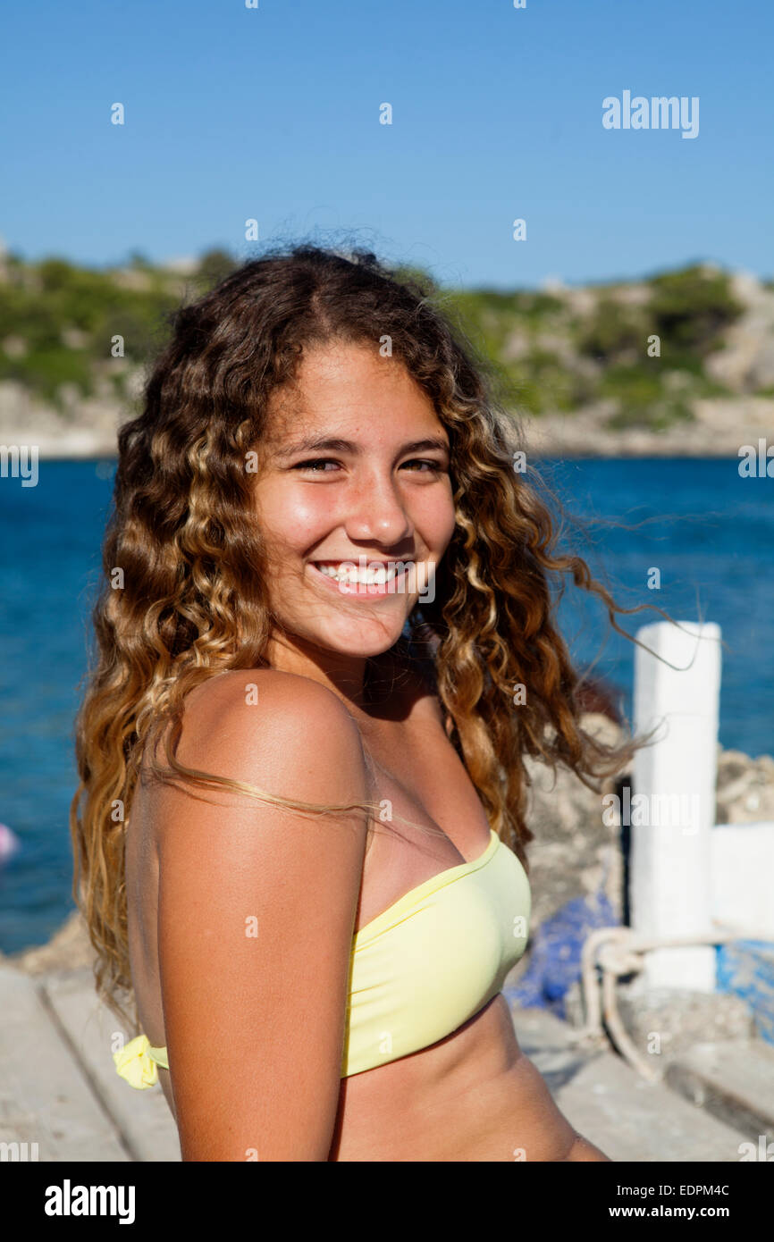 Happy tanned Caucasian teenager girl seated on a wooden dock in a Greek bay Stock Photo